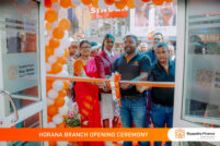 Group of people cutting an orange ribbon at a storefront opening, surrounded by orange and white balloons; banner reads 'Horana Branch Opening Ceremony' with Siyapatha Finance branding visible on the right.